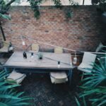Cozy outdoor patio with wooden table and chairs against a rustic brick wall.